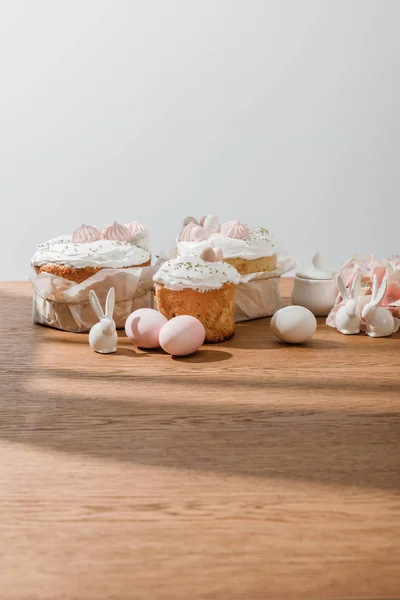 Lapins décoratifs, pétales, œufs de poulet et sucrier près de gâteaux de Pâques isolés sur gris — Photo de stock