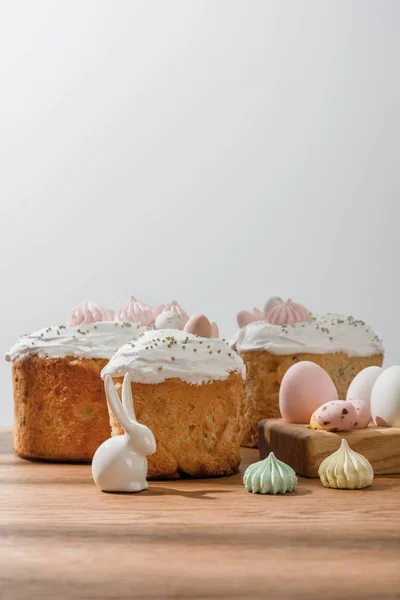 Coelho decorativo, ovos de galinha e codorniz na bandeja de ovos, merengues perto de bolos de Páscoa isolados em cinza — Fotografia de Stock