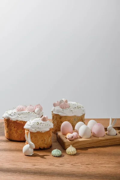 Coelhos decorativos, ovos de galinha e codorniz em bandeja de ovos, merengues e bolos de Páscoa isolados em cinza — Fotografia de Stock
