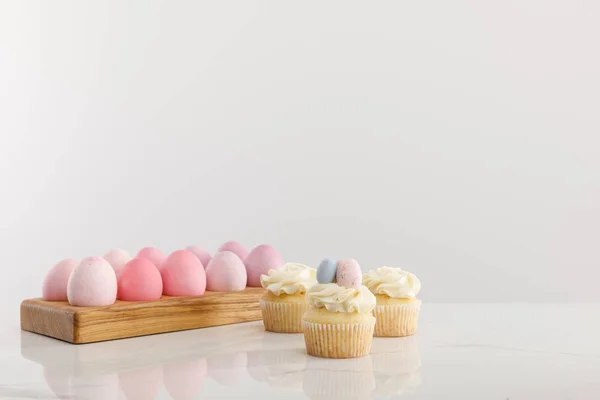 Easter eggs on egg tray with delicious cupcakes isolated on grey background — Stockfoto