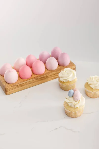 Œufs de Pâques sur plateau d'œufs avec de savoureux cupcakes sur fond gris — Photo de stock