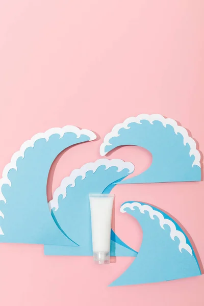 Top view of paper cut sea waves with tube of sunscreen on pink background — Stock Photo