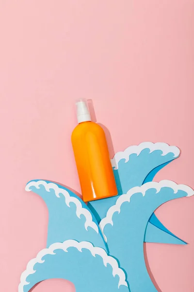 Top view of paper cut sea waves and dispenser bottle of sunscreen on pink — Stock Photo