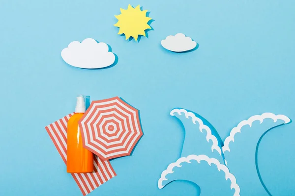 Vue du dessus de la plage de papier découpé avec des vagues et une bouteille de crème solaire sur fond bleu — Photo de stock