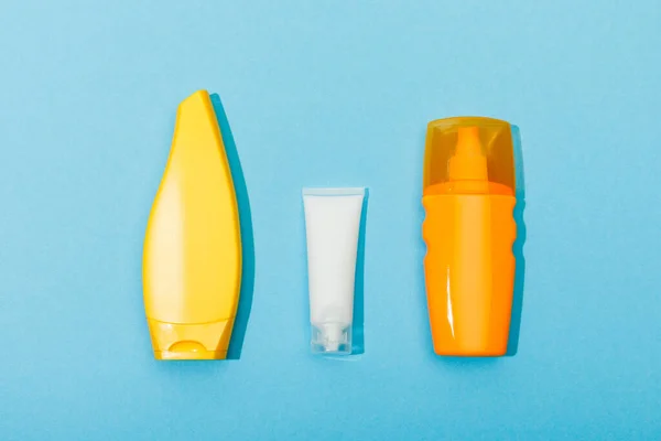 Top view of tubes and dispenser bottle of sunscreen on blue background — Stock Photo