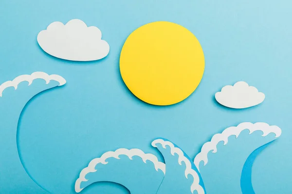 Vue du dessus du papier coupé soleil, nuages et vagues de mer sur bleu — Photo de stock