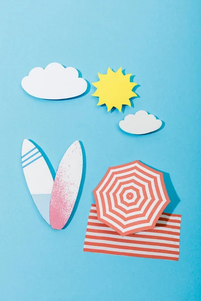 Vue de dessus de la plage de papier découpé avec planches de surf, parapluie et couverture sur fond bleu — Photo de stock