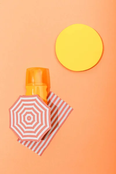 Top view of paper cut sun, beach umbrella and blanket with dispenser bottle of sunscreen on orange — Stock Photo