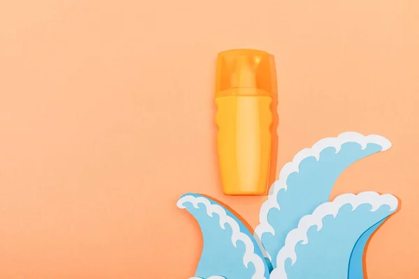 Top view of dispenser bottle of sunscreen with paper cut sea waves on orange background — Stock Photo