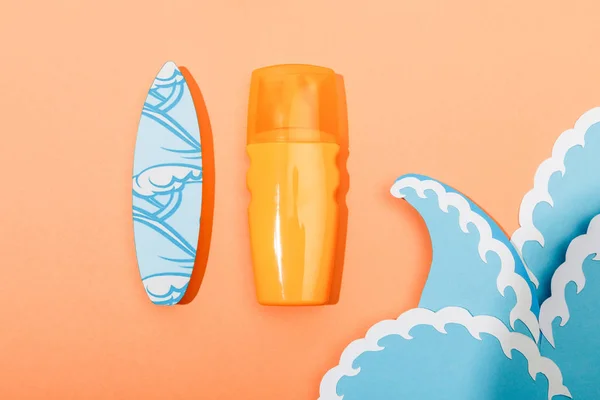 Draufsicht auf Spender Flasche Sonnencreme mit Papier geschnitten Meereswellen und Surfbrett auf orangefarbenem Hintergrund — Stockfoto