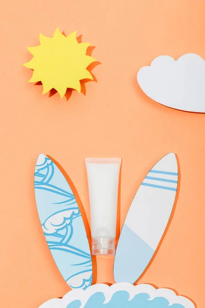 Top view of paper cut sun, cloud, sea wave and surfboards with tube of sunscreen on orange — Stock Photo