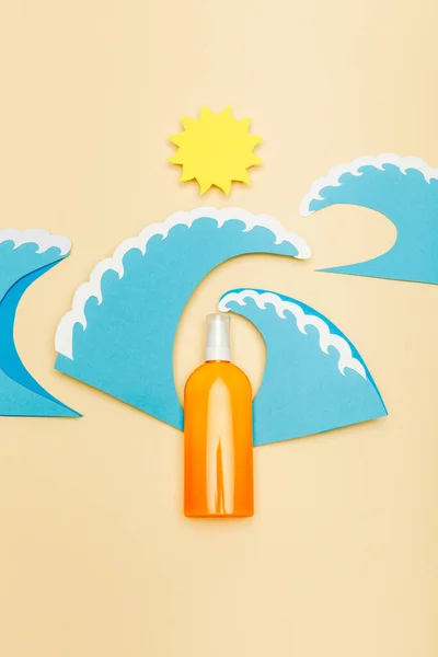 Vue du dessus du papier coupé soleil et vagues de mer avec distributeur bouteille de crème solaire sur beige — Photo de stock