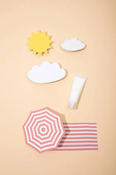 Vista superior do sol de corte de papel, nuvens, guarda-sol de praia e cobertor com tubo de protetor solar em bege — Fotografia de Stock