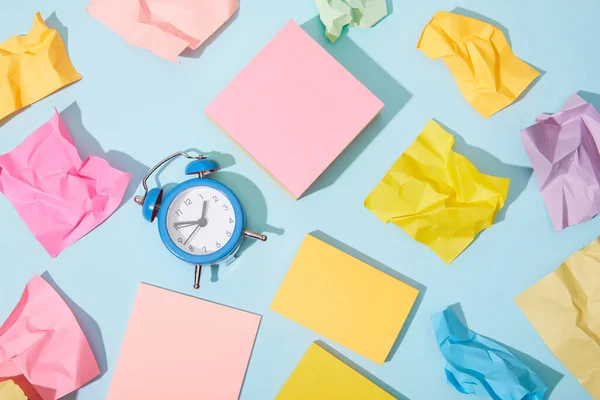 Vista superior del reloj despertador clásico con notas adhesivas de colores sobre fondo azul - foto de stock