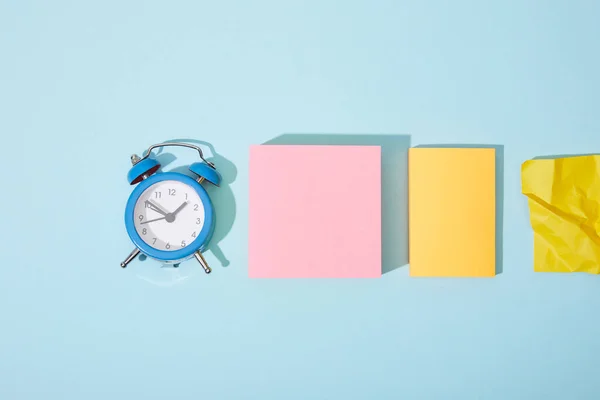 Top view of classic alarm clock with colorful sticky notes on blue background — Stock Photo