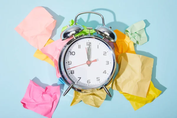 Top view of classic alarm clock with crumpled colorful sticky notes on blue background — Stock Photo