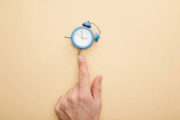 Vista recortada del hombre tocando pequeño reloj despertador sobre fondo beige - foto de stock