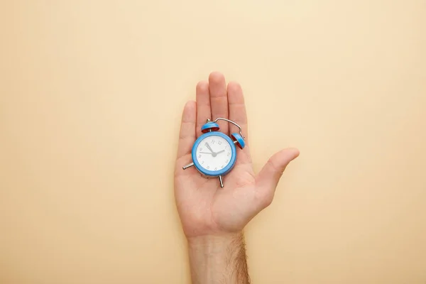 Vista recortada del hombre sosteniendo pequeño reloj despertador sobre fondo beige - foto de stock