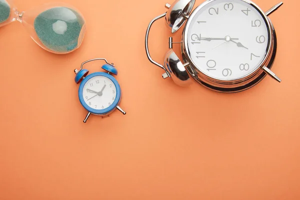 Top view of alarm clocks and hourglass on peach background — Stock Photo