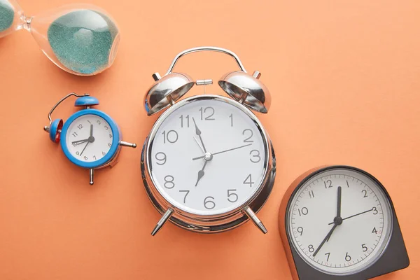 Top view of alarm clocks and hourglass on peach background — Stock Photo