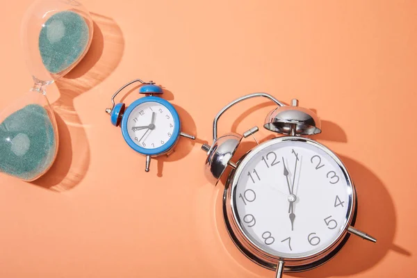 Top view of alarm clocks and hourglass on peach background — Stock Photo