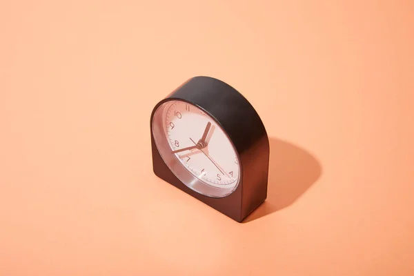 Relógio preto no fundo pêssego com espaço de cópia — Fotografia de Stock