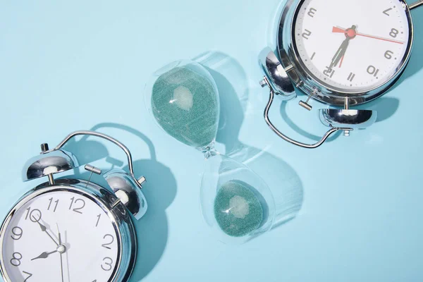 Top view of classic alarm clocks and hourglass on blue background — Stock Photo