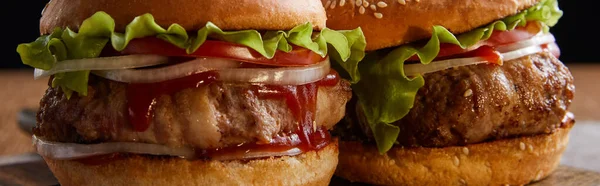 Panoramic shot of two hamburgers on wooden surface isolated on black — Stock Photo