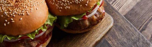 Panoramic high angle shot of burgers on wooden cutting board, cutlery, oil, vinegar and beer bottles — Stock Photo