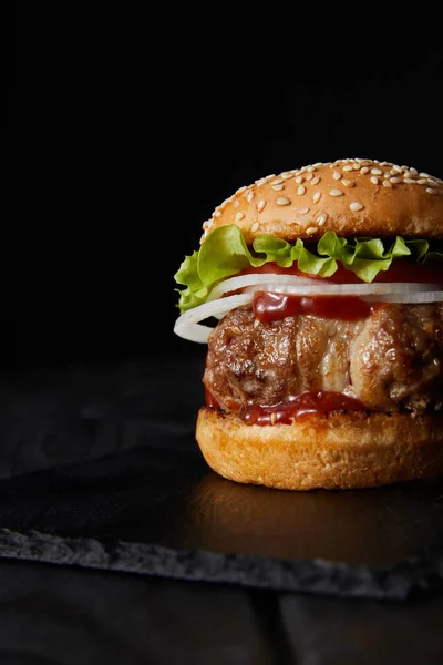 Delicious burger on dark wooden surface isolated on black — Stock Photo