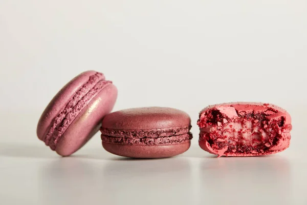 Köstliche ganze und eine gebissene rote französische Makronen auf weißem Hintergrund — Stockfoto
