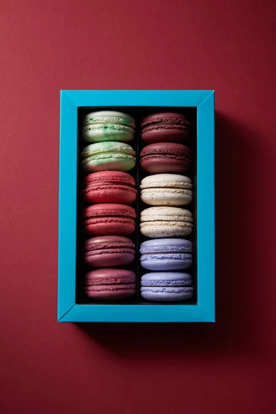 Vista superior de una variedad de deliciosos macarrones franceses coloridos en caja sobre fondo rojo - foto de stock