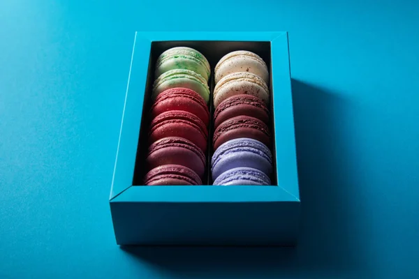 Surtido delicioso colorido macarrones franceses en caja sobre fondo azul - foto de stock