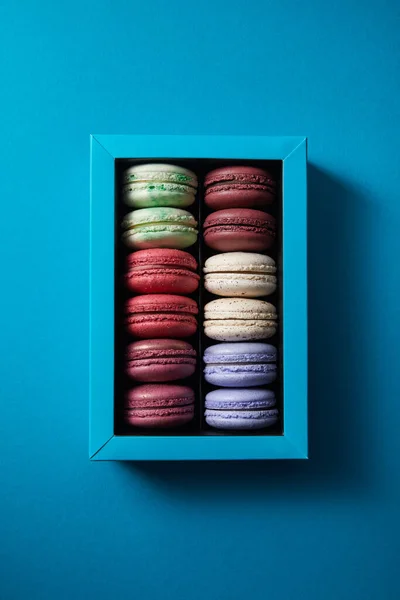 Draufsicht auf verschiedene köstliche bunte französische Makronen in Schachtel auf blauem Hintergrund — Stockfoto