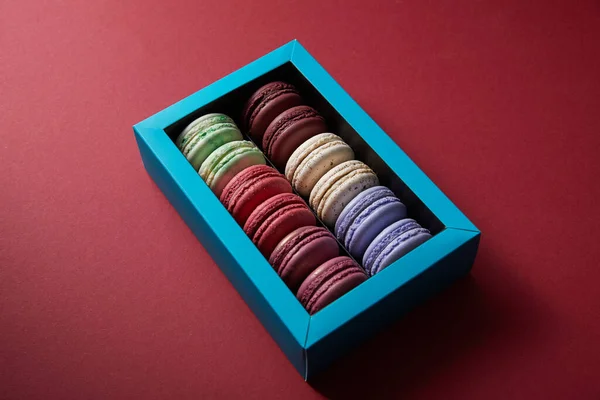 Verschiedene köstliche bunte französische Makronen in Schachtel auf rotem Hintergrund — Stockfoto
