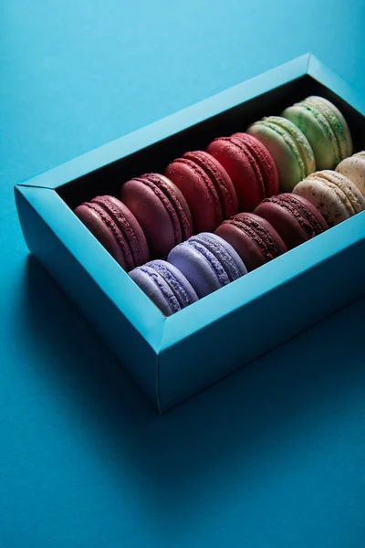 Assorted delicious colorful french macaroons in box on blue background — Stock Photo