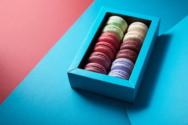 Assorted delicious bitten colorful french macaroons in box on blue and red background — Stock Photo