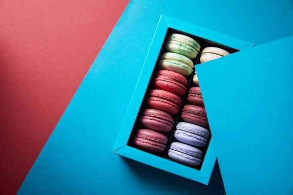 Top view of assorted delicious bitten colorful french macaroons in box on blue and red background — Stock Photo