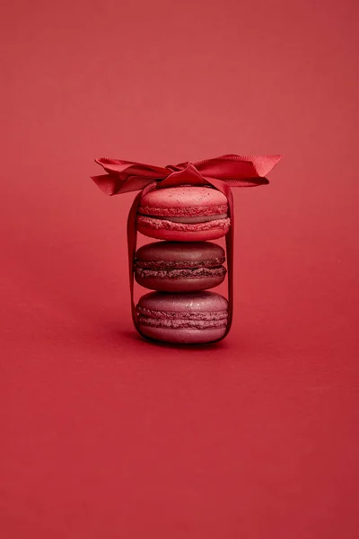 Deliciosos macarrones franceses coloridos envueltos en cinta con lazo sobre fondo rojo - foto de stock