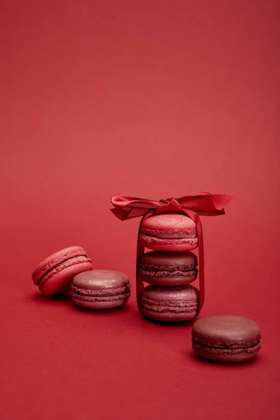 Delicious colorful french macaroons wrapped in ribbon with bow on red background — Stock Photo