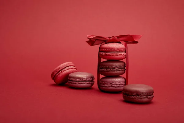 Deliziosi macaron francesi colorati avvolti in nastro con fiocco su sfondo rosso — Foto stock