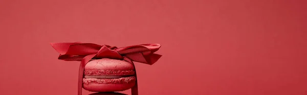 Delicious colorful french macaroon wrapped in ribbon with bow isolated on red, panoramic shot — Stock Photo