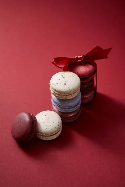 Assortiti deliziosi macaron francesi colorati con fiocco su sfondo rosso — Foto stock