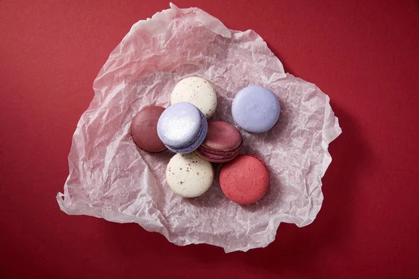 Vista dall'alto di deliziosi macaron francesi colorati assortiti su carta spiegazzata su sfondo rosso — Foto stock