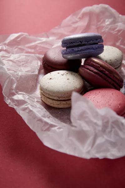Close up view of assorted delicious colorful french macaroons on crumpled paper on red background — Stock Photo