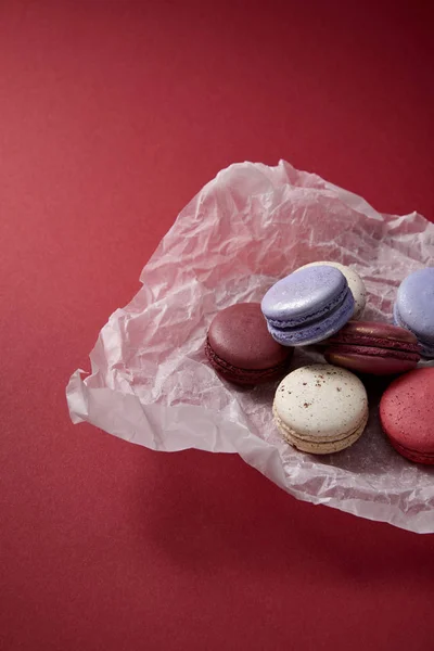 Sortidas deliciosos macaroons franceses coloridos em papel amassado no fundo vermelho — Fotografia de Stock