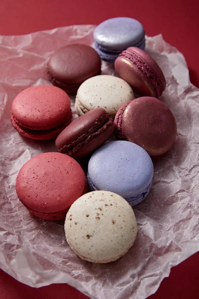 Vista de perto de sortidas deliciosos macaroons franceses coloridos em papel amassado no fundo vermelho — Fotografia de Stock