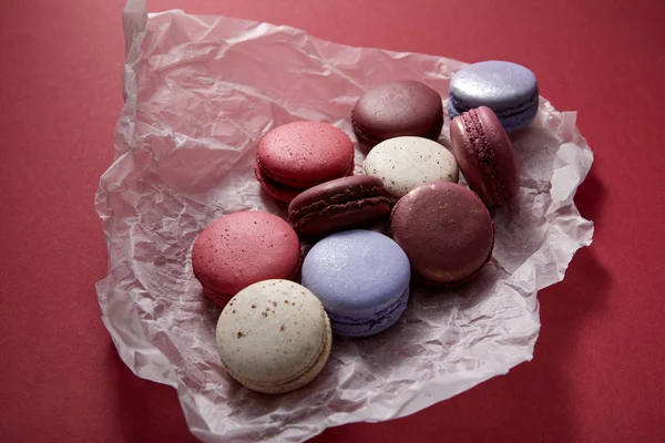 Assorted delicious colorful french macaroons on crumpled paper on red background — Stock Photo