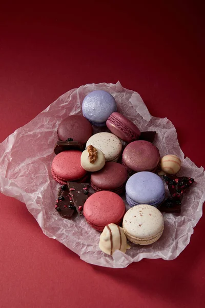 Macarons français colorés sur papier froissé avec du chocolat sur fond rouge — Photo de stock