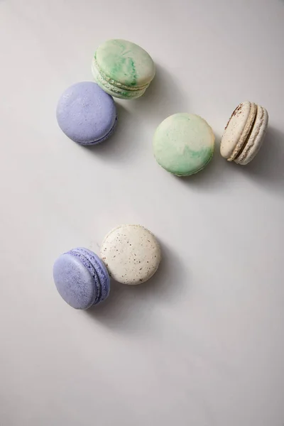 Vista superior de uma variedade de deliciosos macaroons verdes, violetas e brancos franceses no fundo cinza — Fotografia de Stock